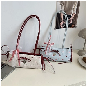 Detail of a chic shoulder bag featuring red polka dots, lace ribbons, and a heart pendant