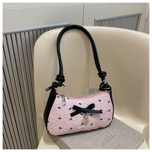 Détail du sac croissant plissé rose avec nœud noir et pendentif cœur posé sur un livre