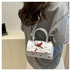 Detail of blue cylinder bag with red bow, lace trim, and heart pendant on a desk
