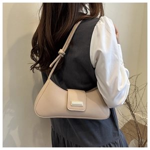 Detail of a cream faux leather baguette bag with a stylish knot handle and magnetic flap