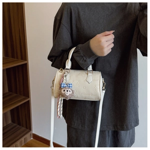 Detail of white cylinder handbag with bear embossed pattern and plush charm pendant