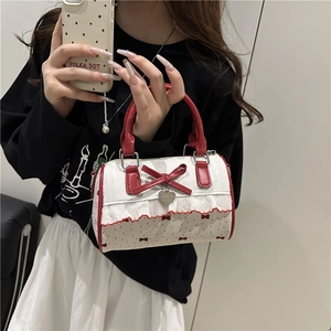 Polka dot cylinder handbag with red leather bow and ruffle trim held by a model