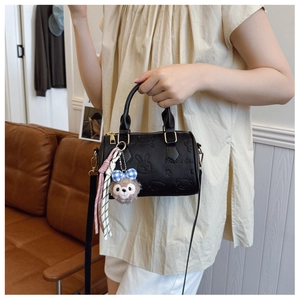 Detail of black embossed boston bag featuring cartoon patterns and plush bear charm