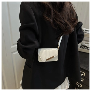 Detail einer weißen Mini-Ledertasche mit Goldbeschlägen über einem schwarzen Blazer