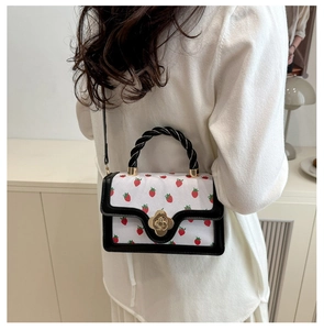 Detail showing white strawberry print crossbody bag with gold flower clasp and black handle