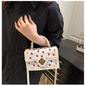 Close-up of strawberry print handbag with floral metal clasp and twisted handle