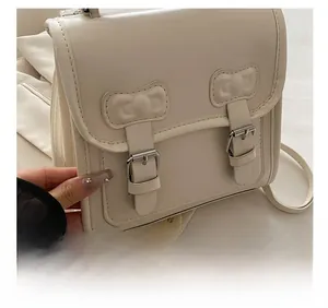 Détail de la sacoche en cuir PU crème avec boucles métalliques et nœud décoratif élégant