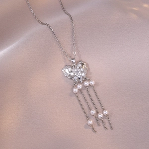 Collier cœur en zircon avec pompons de perles élégants sur fond de tissu en soie rose