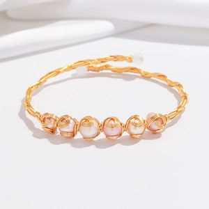 Detail eines handgefertigten Golddraht-Armreifs mit sechs natürlichen rosa Perlen