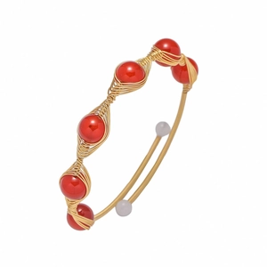 Detail of handmade gold wire-wrapped open cuff bracelet with vibrant red beads