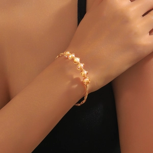 Detailaufnahme eines handgefertigten Golddraht-Armbands mit sechs rosa Perlen am Handgelenk