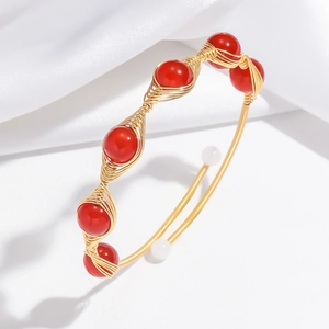 Detail view of handmade gold wire-wrapped bangle with red beads on silk background