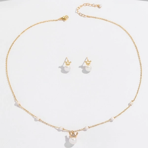 Detailed view of crown-shaped gold necklace and pearl earrings jewelry set