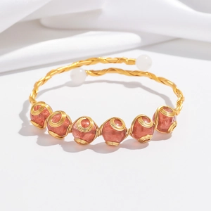 Detail eines handgefertigten Armreifs mit Golddraht, roten Perlen und weißen Perlen