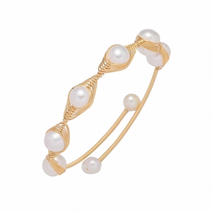 Macro detail of hand-wrapped gold wire texture and white pearls on an open bangle