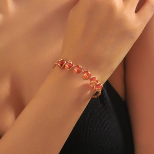 Nahaufnahme eines Perlenarmbands mit Erdbeerquarz und goldener Drahtwickeltechnik
