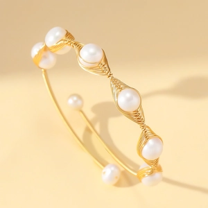 Detail of gold wire wrapped bangle featuring white pearls in an elegant open design