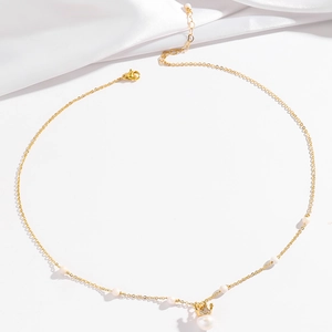 Detailed close-up of golden crown pendant with white pearl on minimalist necklace