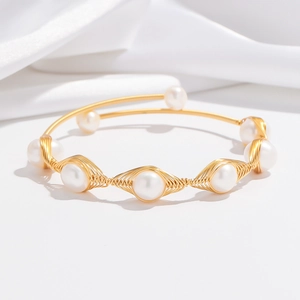 Detail of woven gold wire craftsmanship and white pearls on an elegant open bangle