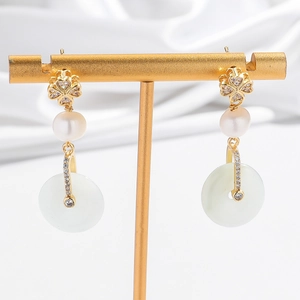 Detail of elegant earrings with diamond clover, white pearl and green jade ring