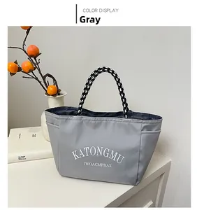 Detail of grey nylon tote bag with woven handles and KATONGMU text on white background
