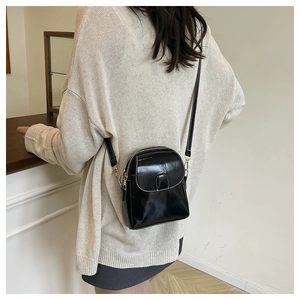 Detail of a black glossy PU leather crossbody bag with gold chain and dual zipper closures