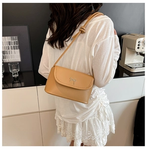 Sac bandoulière beige chic avec nœud argenté porté par un mannequin dans un décor urbain