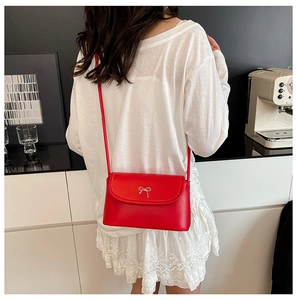 Détail du sac bandoulière rouge avec nœud argenté porté sur une jupe en dentelle blanche