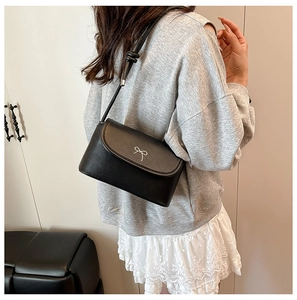 Détail d'un sac bandoulière en cuir noir avec un nœud en métal argenté sur mannequin