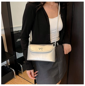 Détail d'un sac bandoulière argenté brillant avec un nœud métallique décoratif sur le rabat