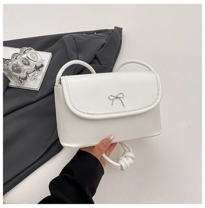 Gros plan du sac bandoulière blanc avec boucle nœud argenté sur fond de costume gris