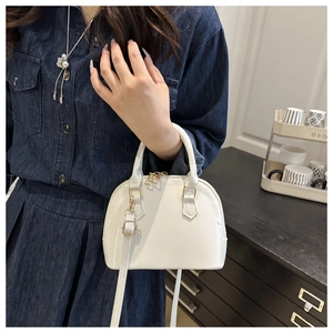 Close-up of a white shell-shaped patent leather crossbody bag with golden hardware