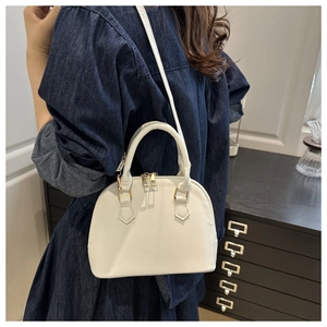Detailed view of white shell-shaped leather bag with golden zippers and double handles