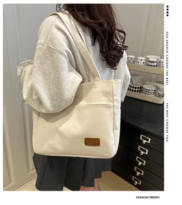 Detail view of cream canvas tote bag with brown leather logo patch and outer pocket