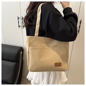Detail view of a beige canvas tote bag with a front pocket and brown leather logo tag