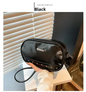 Close-up of black leather crossbody bag featuring silver rivets and metal brand plaque