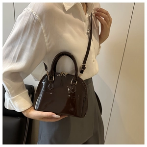 Close-up of a dark brown glossy patent leather shell bag with gold zipper detail