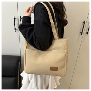 Detail view of beige canvas tote bag with outer pocket and brown leather logo tag