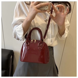 Detail of a shiny dark red shell-shaped handbag with golden hardware and long shoulder strap