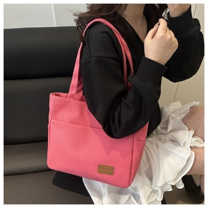 Close-up of bright pink canvas tote bag featuring brown leather logo and front pocket