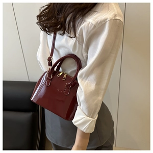 Detail of burgundy patent leather shell bag with adjustable strap and dual zipper closure