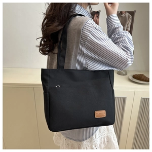 Detail of black canvas tote bag showing front pocket and brown leather logo patch
