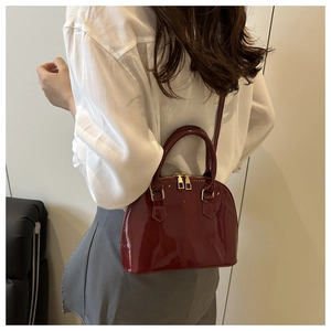 Fashionable dark red shell bag in glossy patent leather worn by a model in a casual setting