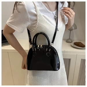 Glossy black patent leather shell bag with gold hardware shown on a shoulder strap