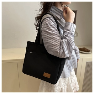 Close-up of black canvas tote bag featuring a front zipper pocket and brown leather patch