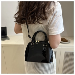 Fashionable black patent leather shell bag shown with a white mesh dress on model