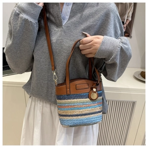 Detail of color-block woven straw bucket bag with brown leather trim and golden hardware