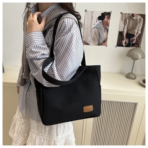 Detail of black canvas tote bag with brown leather logo and side pocket on a model