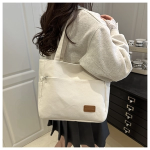 Detail of cream canvas tote bag showing the front zipper pocket and side pocket on a model