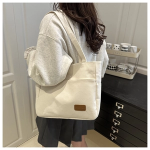 Detail of off-white canvas tote bag with front pocket and brown leather brand patch